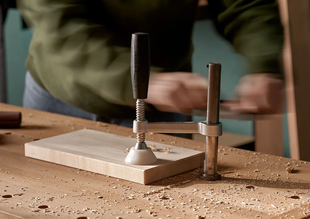 En bänkspännare ligger på en arbetsbänk, Person i grön tröja i bakgrunden