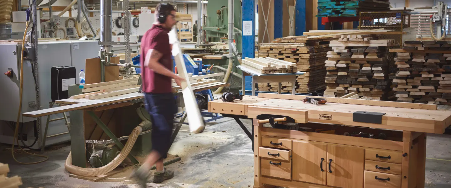 En kille i en verkstad bär på en träplanka